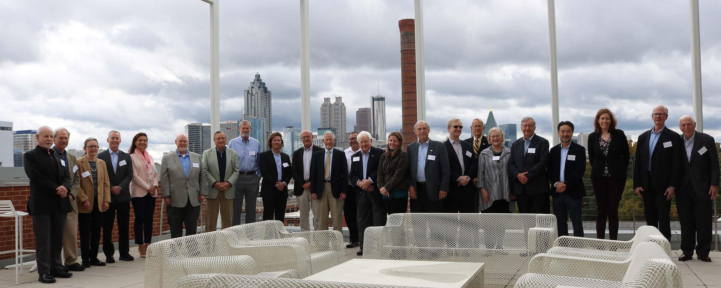 The COS Advisory Board members in a line on top of the Kendeda building, with the overcast Atlanta skyline behind them