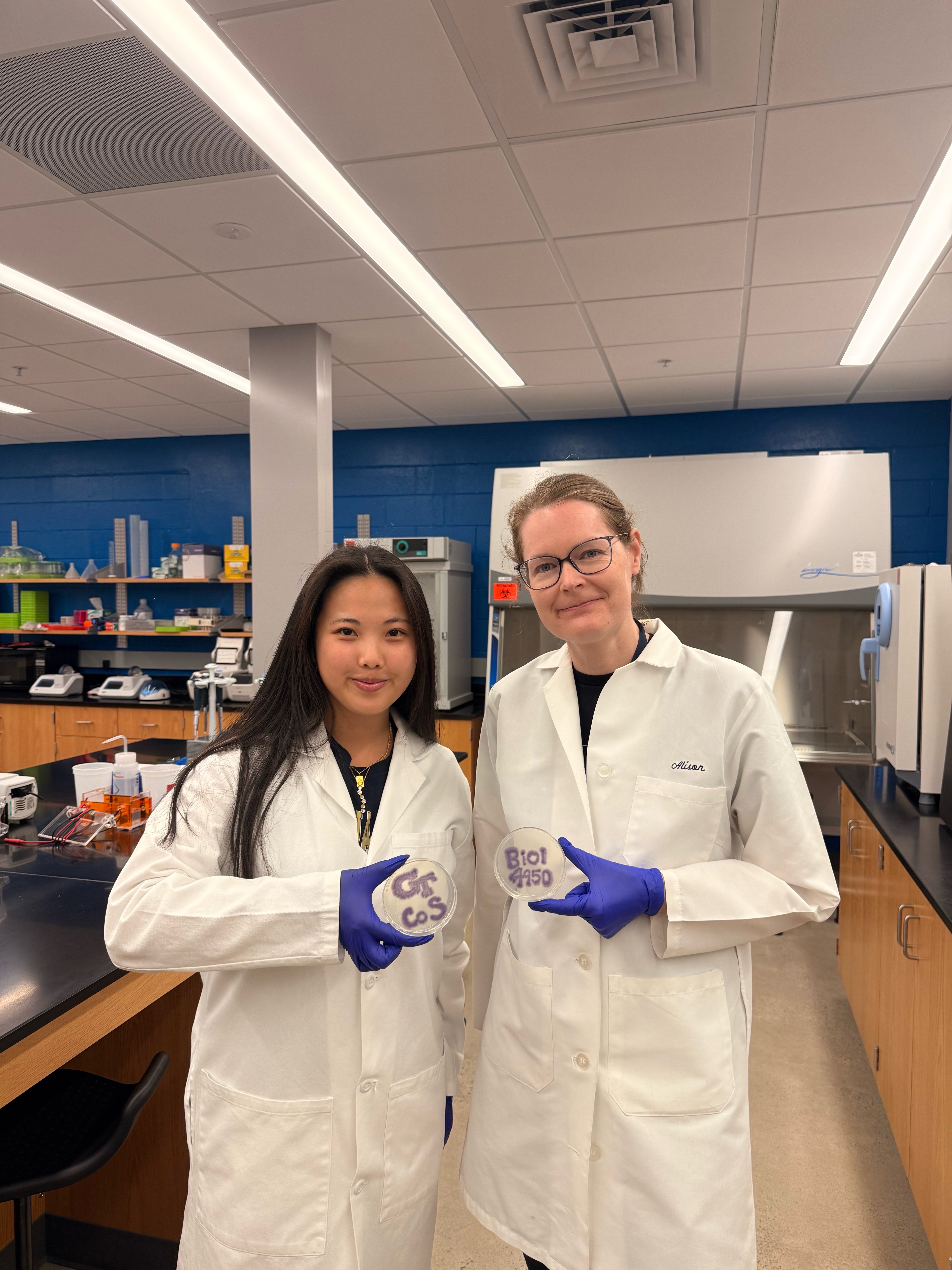 Grace Tang (Left) and Alison Onstine (Right) holding bacteria plates that spell 